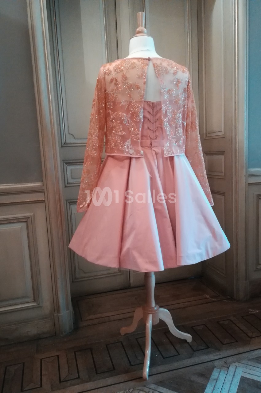 Robe rose avec jupe évasée et haut brodé transparent, présentée sur un mannequin dans un intérieur élégant.