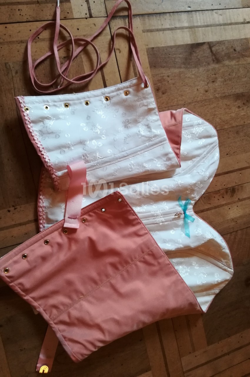 Corset en tissu rose et blanc à motifs floraux, avec lacets et œillets dorés, posé sur un sol en bois.