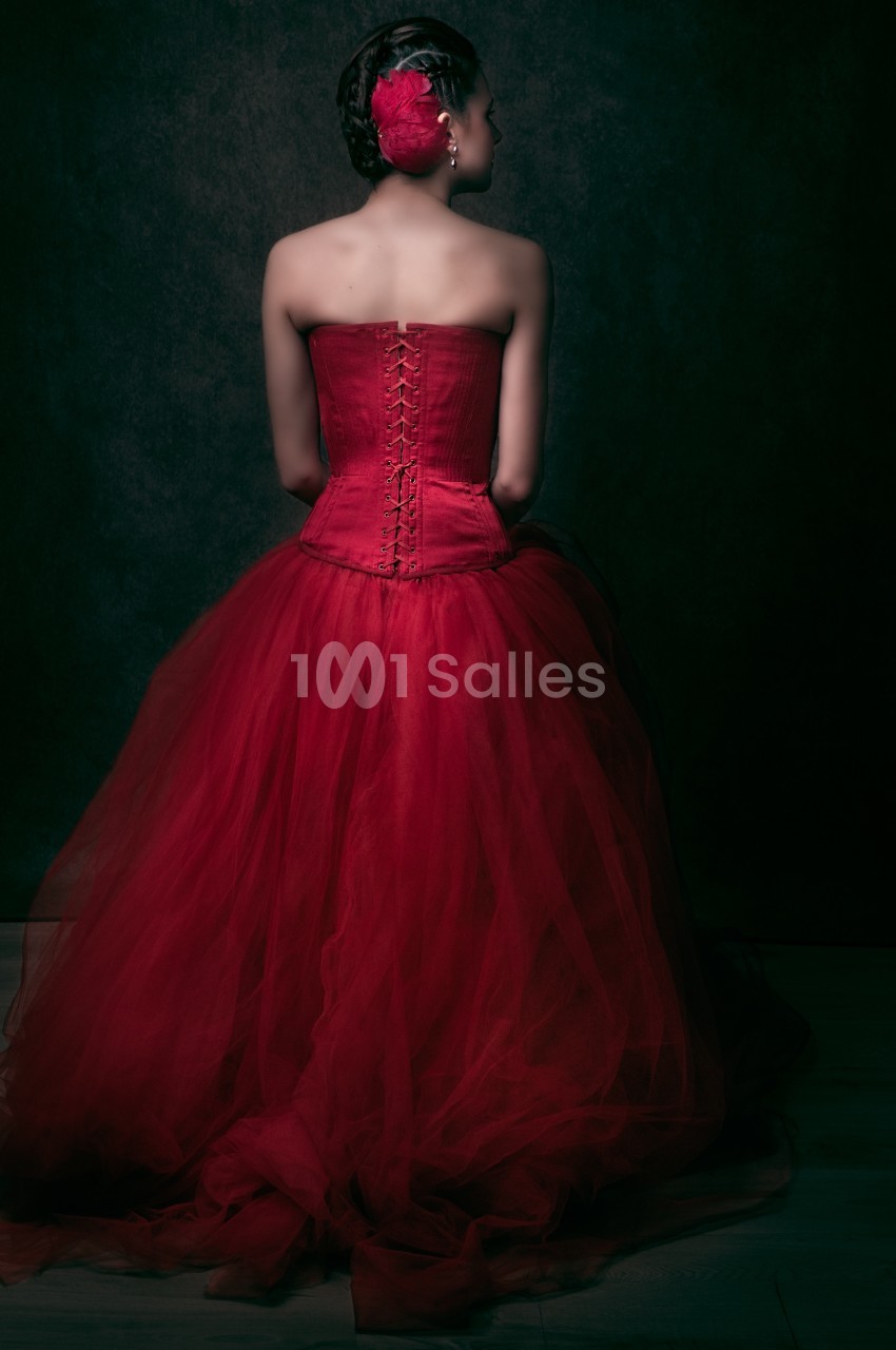 Femme de dos portant une robe rouge corsetée avec une jupe en tulle, coiffée d'une fleur assortie dans les cheveux.