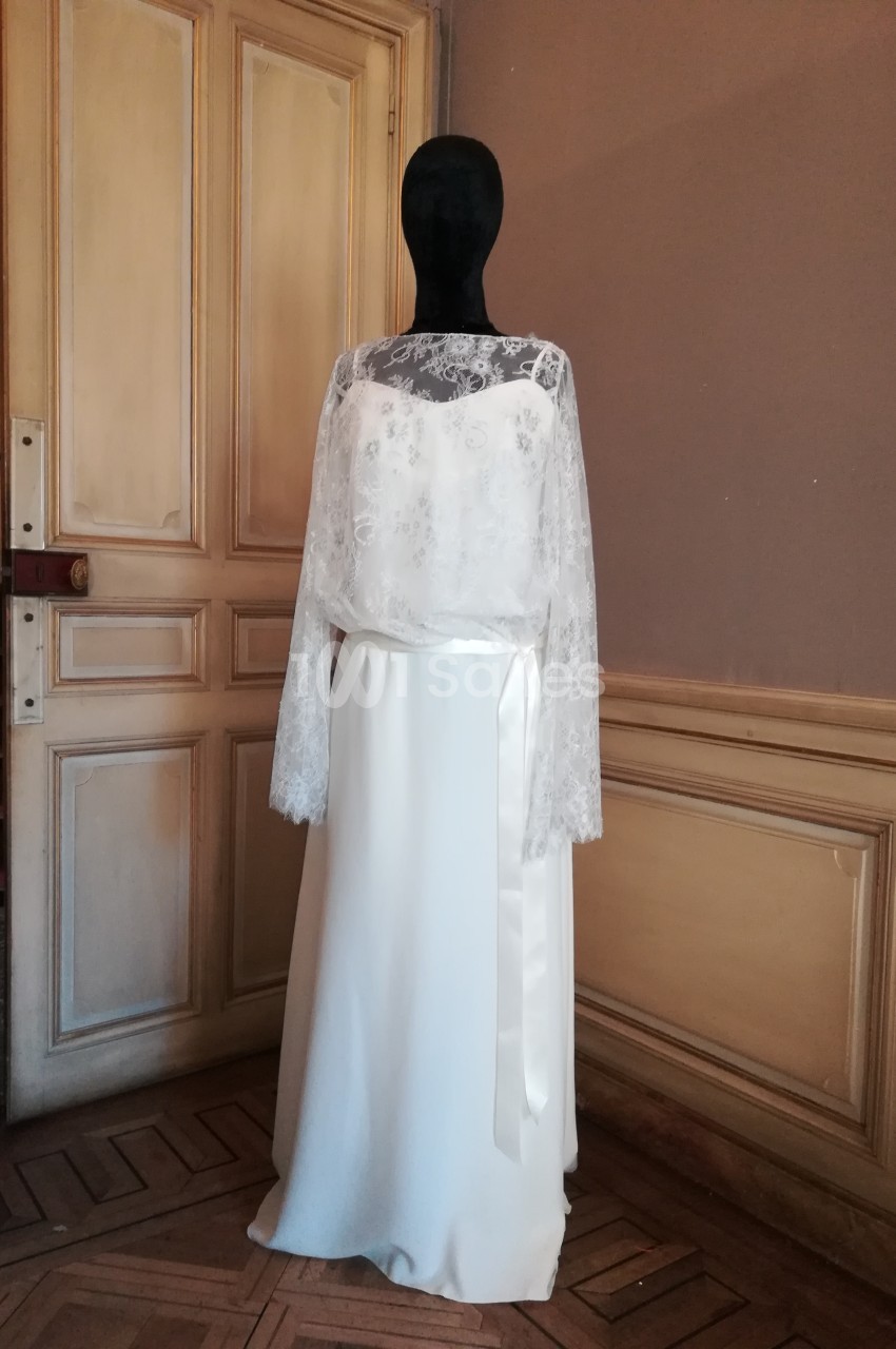 Robe de mariée blanche avec haut en dentelle et manches longues, exposée sur un mannequin dans une pièce ancienne.