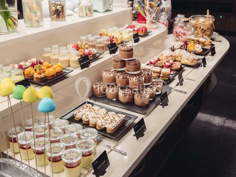 Buffet de desserts variés avec verrines, pâtisseries, fruits et bonbons disposés sur un comptoir lumineux.
