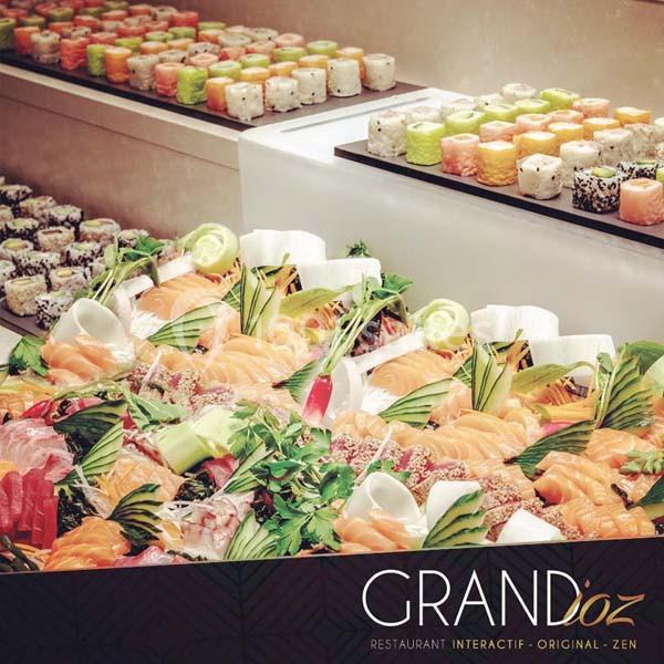 Plateau de sushis variés avec des tranches de poisson cru, légumes et herbes, présenté sur un buffet.