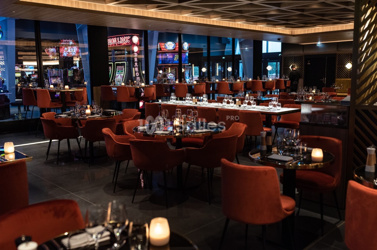 Salle de restaurant élégante avec des tables dressées, des chaises rouges et un éclairage tamisé, vue sur des machines à…