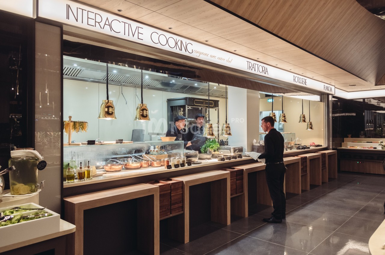 Un homme commande devant un comptoir de cuisine interactive avec des chefs préparant des plats en arrière-plan.
