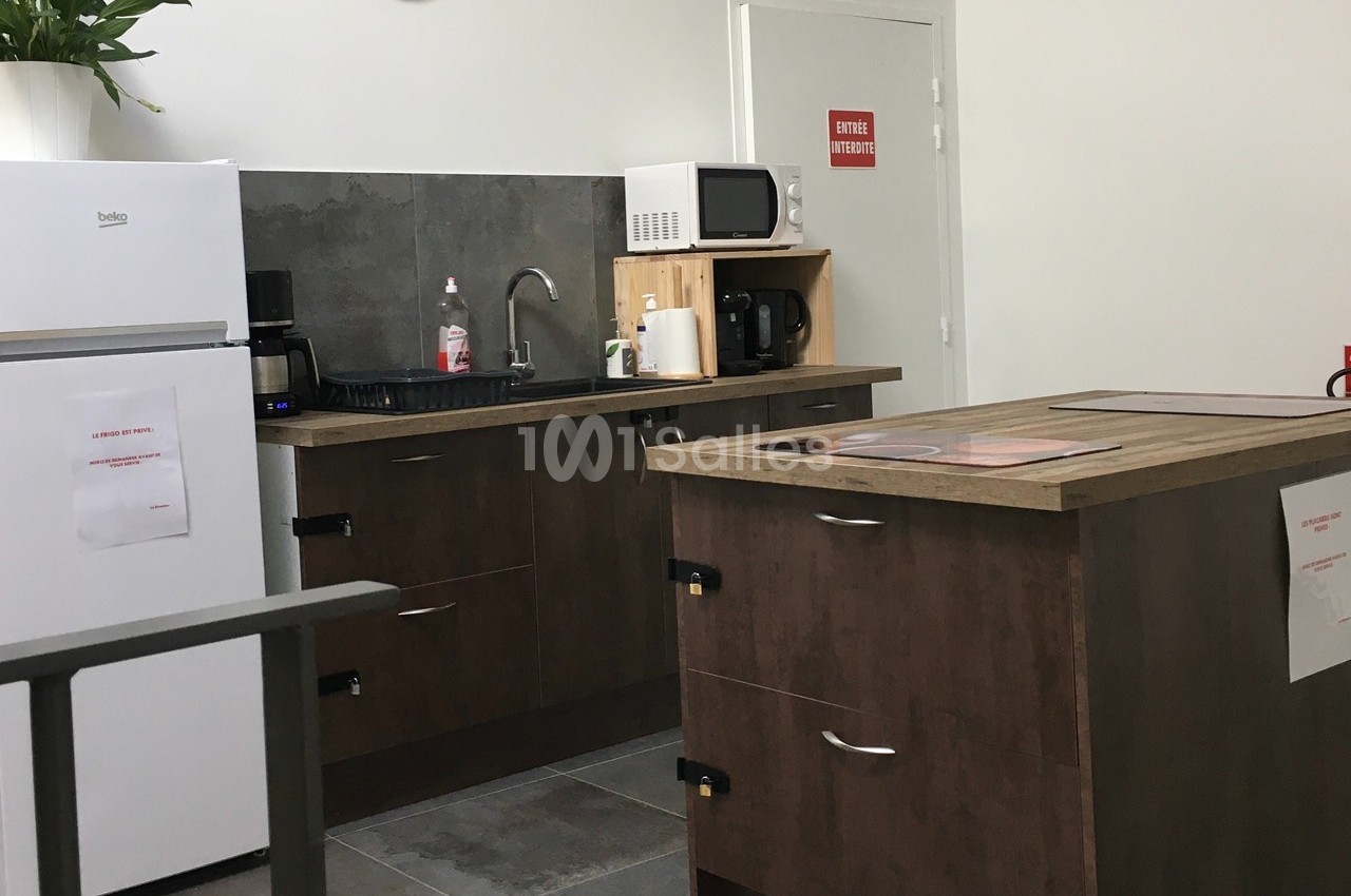 Cuisine équipée avec réfrigérateur, micro-ondes, cafetière, évier et plan de travail en bois, décor sobre et fonctionnel.