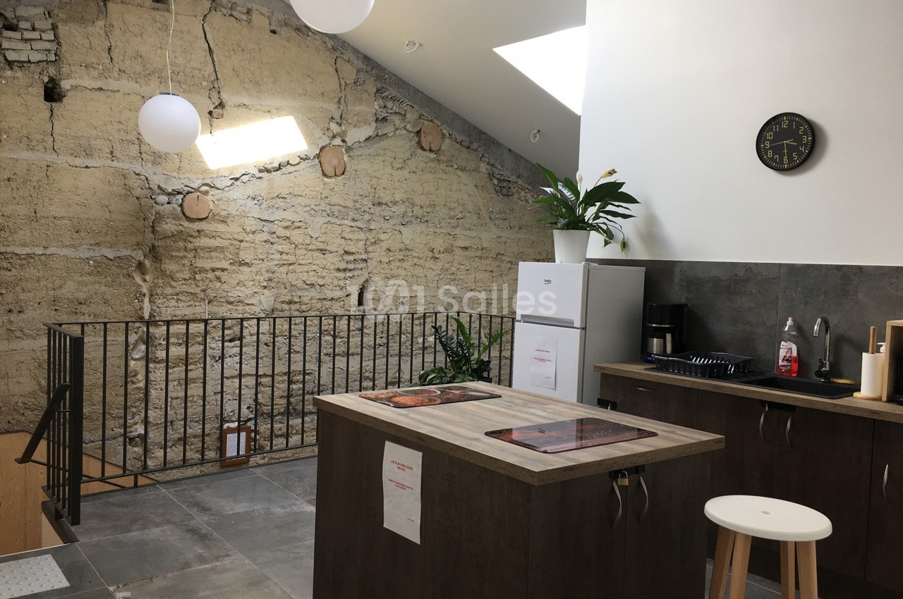 Cuisine moderne avec îlot central, mur en pierre apparente, plafond incliné et éclairage naturel par une fenêtre de toit.