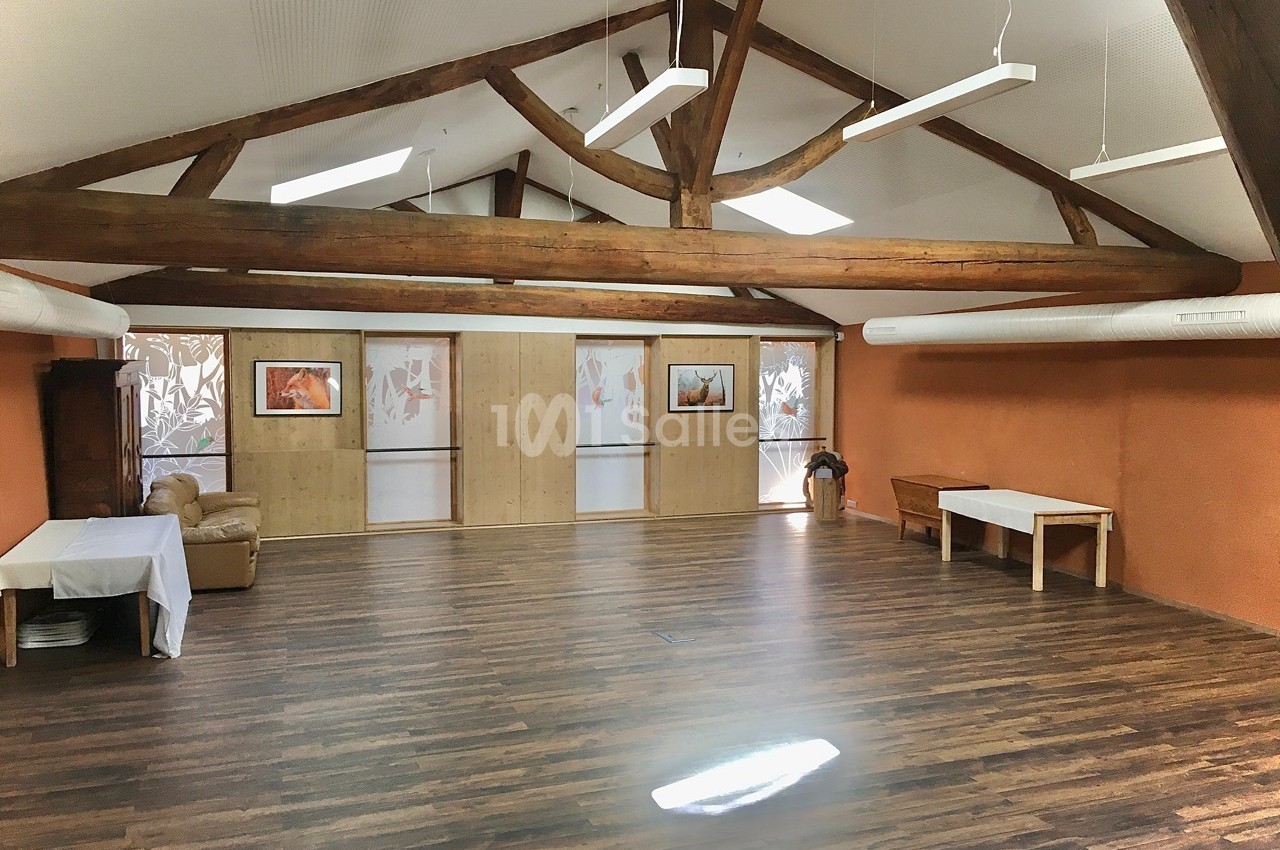 Salle spacieuse avec parquet, murs orange, poutres apparentes et mobilier minimaliste, éclairée par des fenêtres et des…