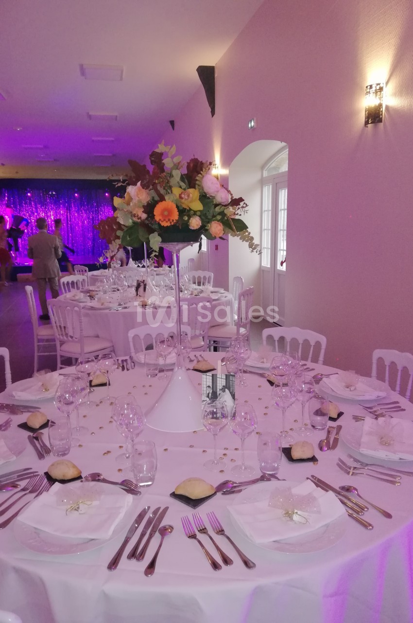 Salle de réception décorée avec des tables rondes élégantes, nappes blanches et centre de table floral.