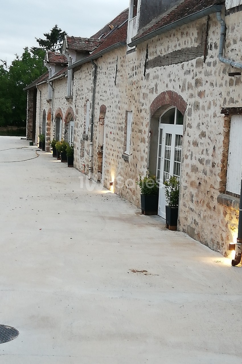 Façade en pierre d'une maison avec des portes vitrées, des plantes en pots et un éclairage extérieur au sol.