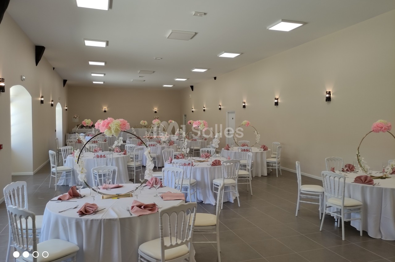 Salle de réception décorée avec des tables rondes, nappes blanches, serviettes roses et centres de table fleuris.