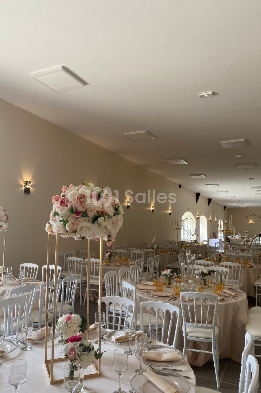Salle de réception élégamment décorée avec des tables rondes, nappes blanches et centres de table fleuris.