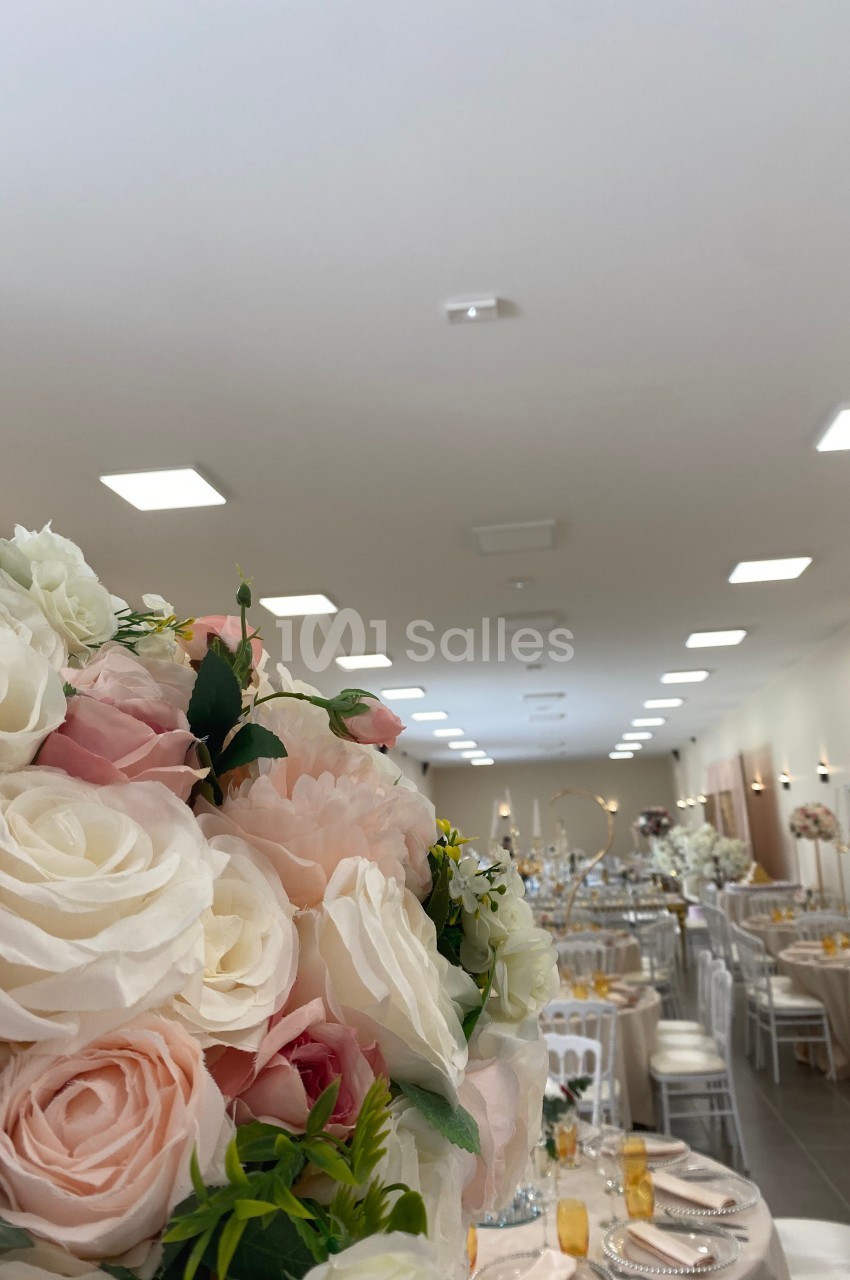Salle de réception décorée avec des tables dressées et un bouquet de roses blanches et roses au premier plan.