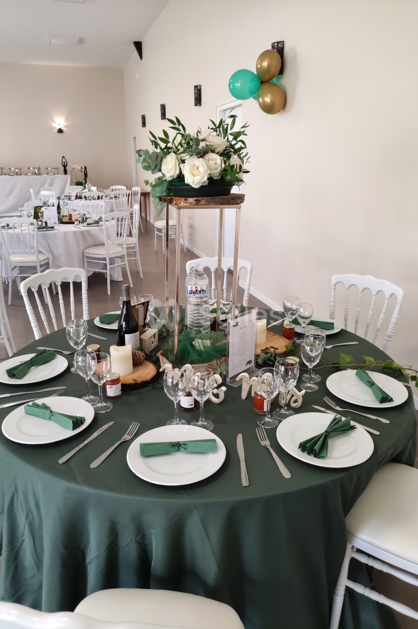 Table de réception décorée avec une nappe verte, vaisselle blanche, centre de table floral et accessoires festifs.