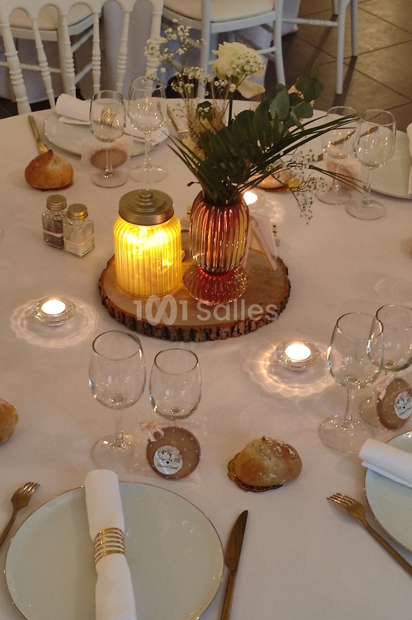 Table de réception décorée avec des bougies, des fleurs, des verres et des couverts dorés sur une nappe blanche.