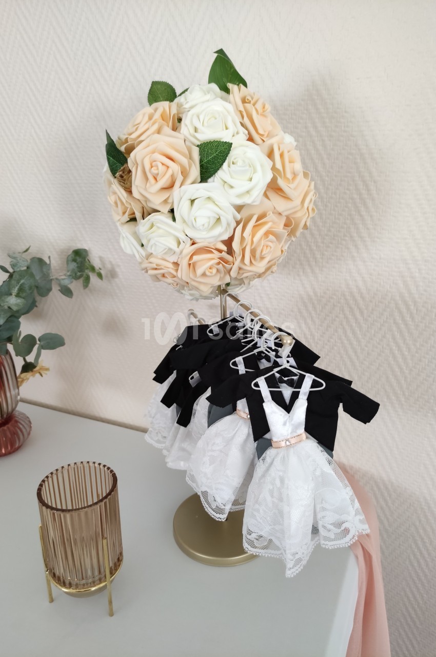 Bouquet de roses crème et pêche sur un support doré, entouré de petites robes blanches suspendues.