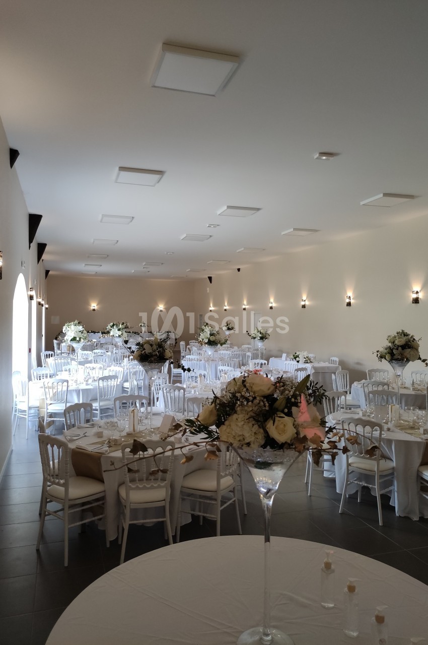 Salle de réception élégamment décorée avec des tables rondes, des nappes blanches et des arrangements floraux.