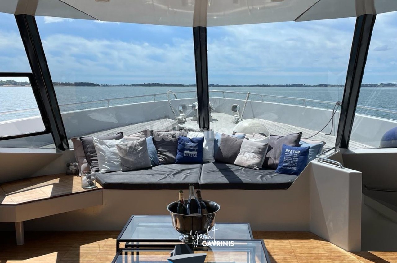 Salon extérieur d'un yacht avec banquette garnie de coussins, table basse et vue sur la mer sous un ciel dégagé.