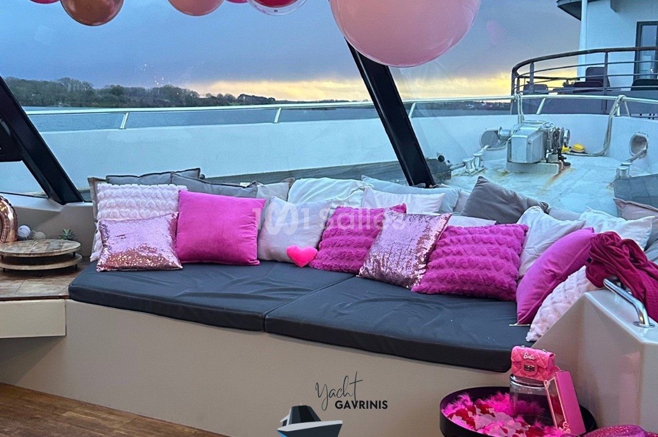 Banquette extérieure décorée de coussins roses et ballons, sur un yacht au coucher du soleil.