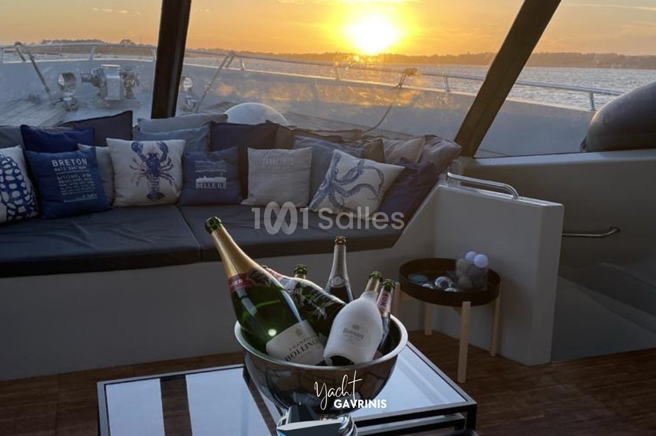 Salon extérieur d'un yacht au coucher du soleil, avec un seau de bouteilles de champagne sur une table basse.