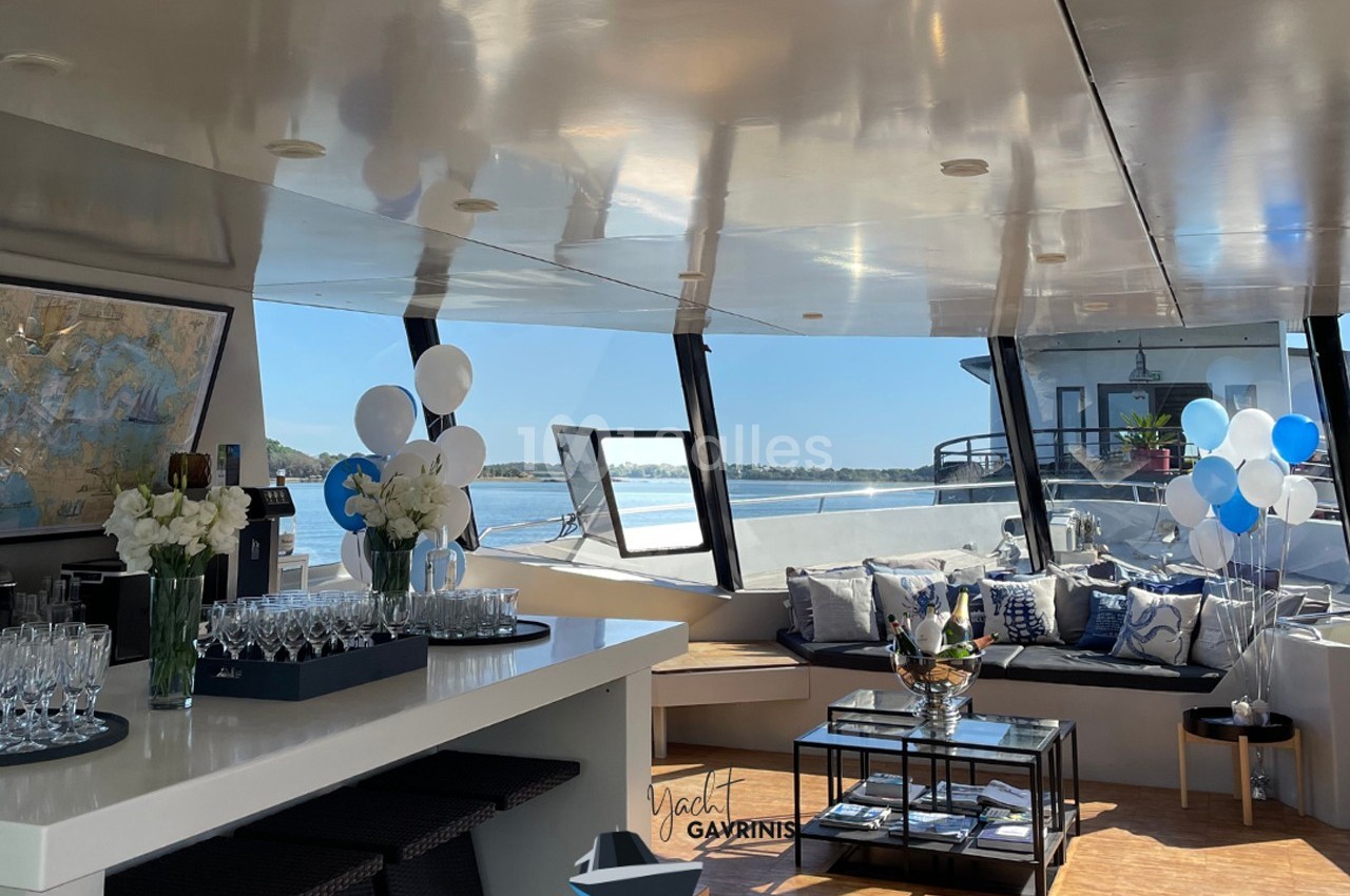 Espace intérieur d'un yacht avec bar, canapés, décorations festives et vue sur l'eau par des baies vitrées.
