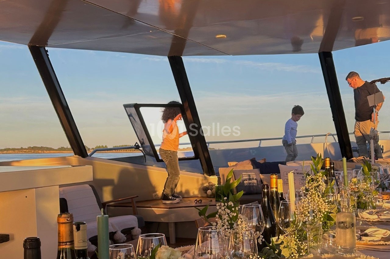 Deux enfants jouent sur le pont d'un bateau au coucher du soleil, avec une table dressée au premier plan.
