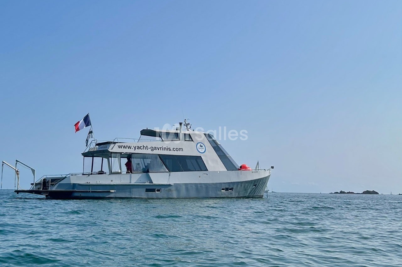 Bateau moderne avec un drapeau français naviguant sur une mer calme sous un ciel dégagé.
