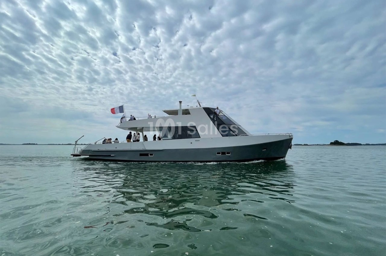 Bateau moderne naviguant sur une eau calme sous un ciel partiellement nuageux, avec des passagers à bord.