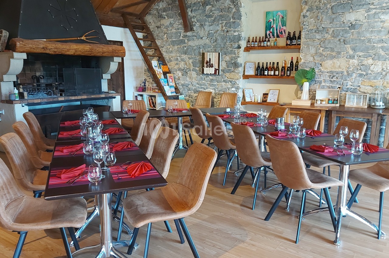 Salle de restaurant avec tables dressées, chaises en cuir, murs en pierre et cheminée décorative.
