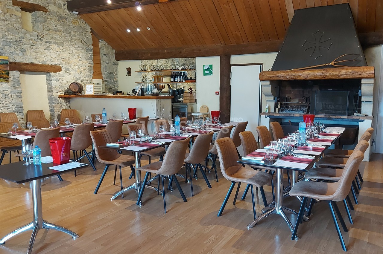 Salle de restaurant avec tables dressées, chaises en bois, cheminée en pierre et décor rustique.
