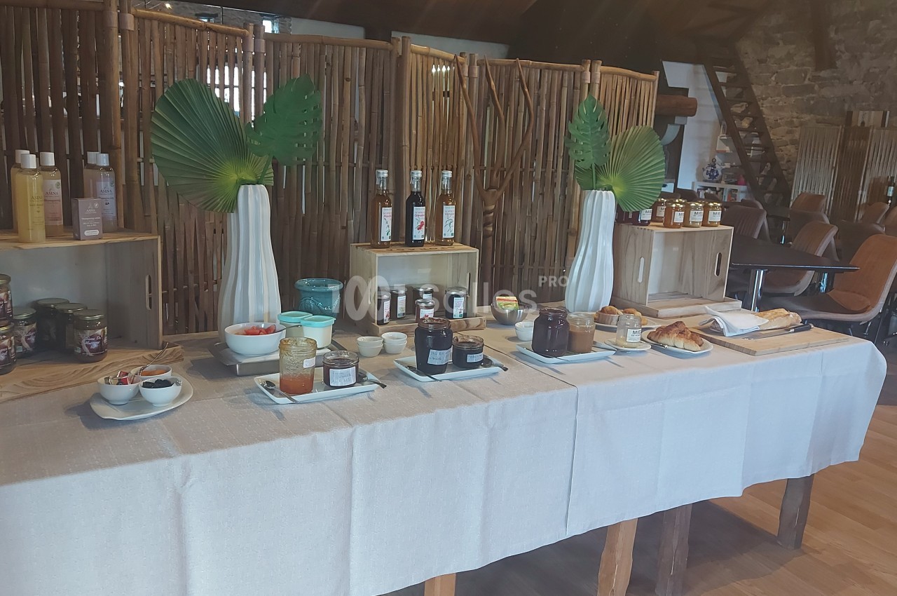 Buffet de petit-déjeuner avec confitures, pains, boissons et décorations tropicales dans une salle en bois.