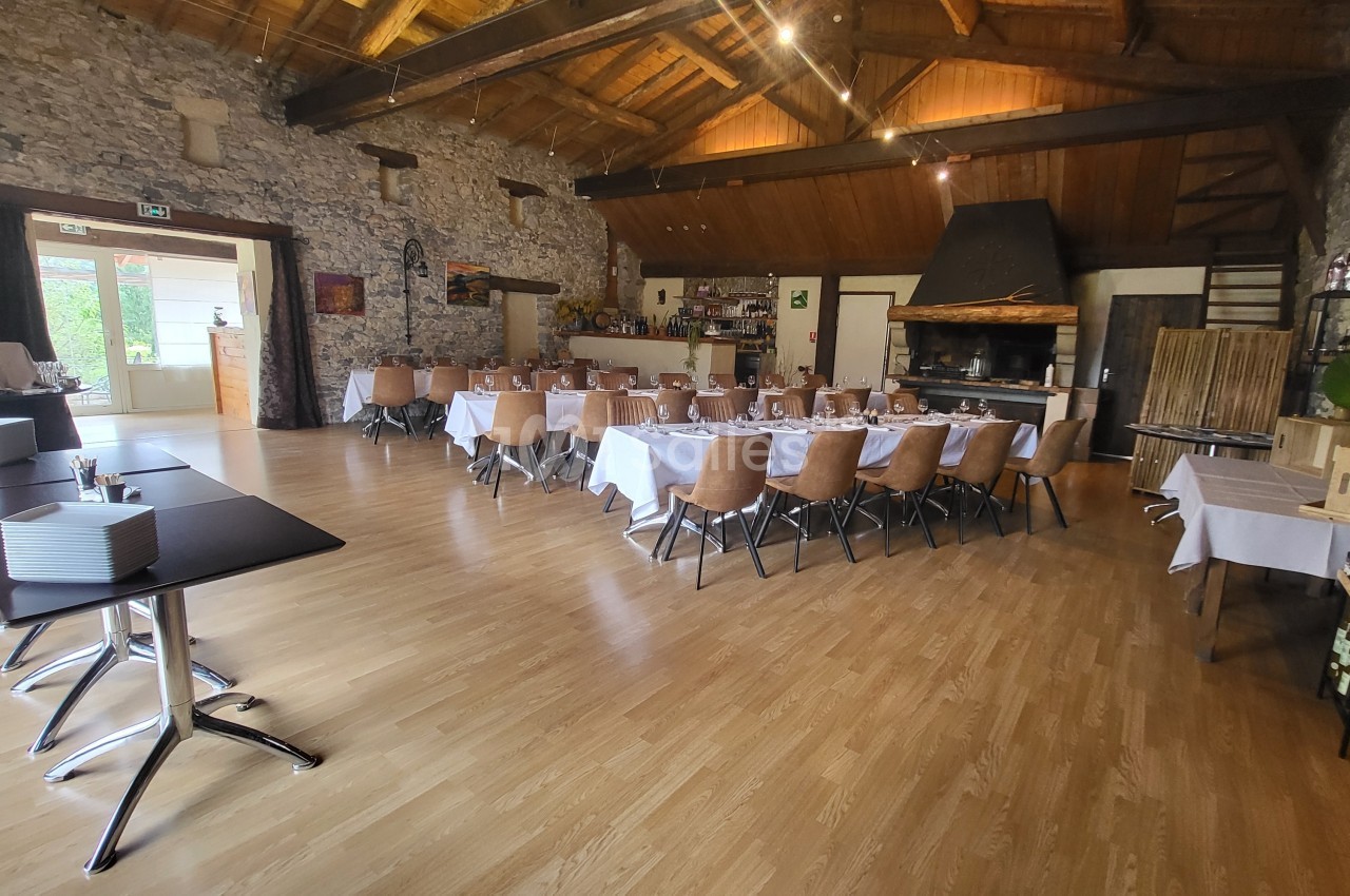 Salle de réception avec tables dressées, chaises en bois, murs en pierre et plafond en bois, éclairée par des lumières et…