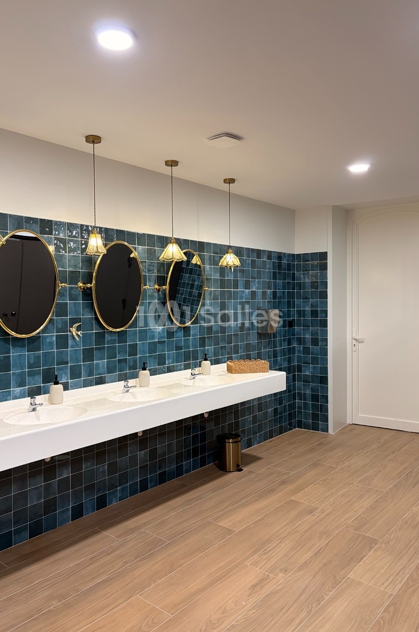 Salle de bain moderne avec carrelage bleu, trois miroirs ronds, un plan vasque blanc et un sol en bois clair.