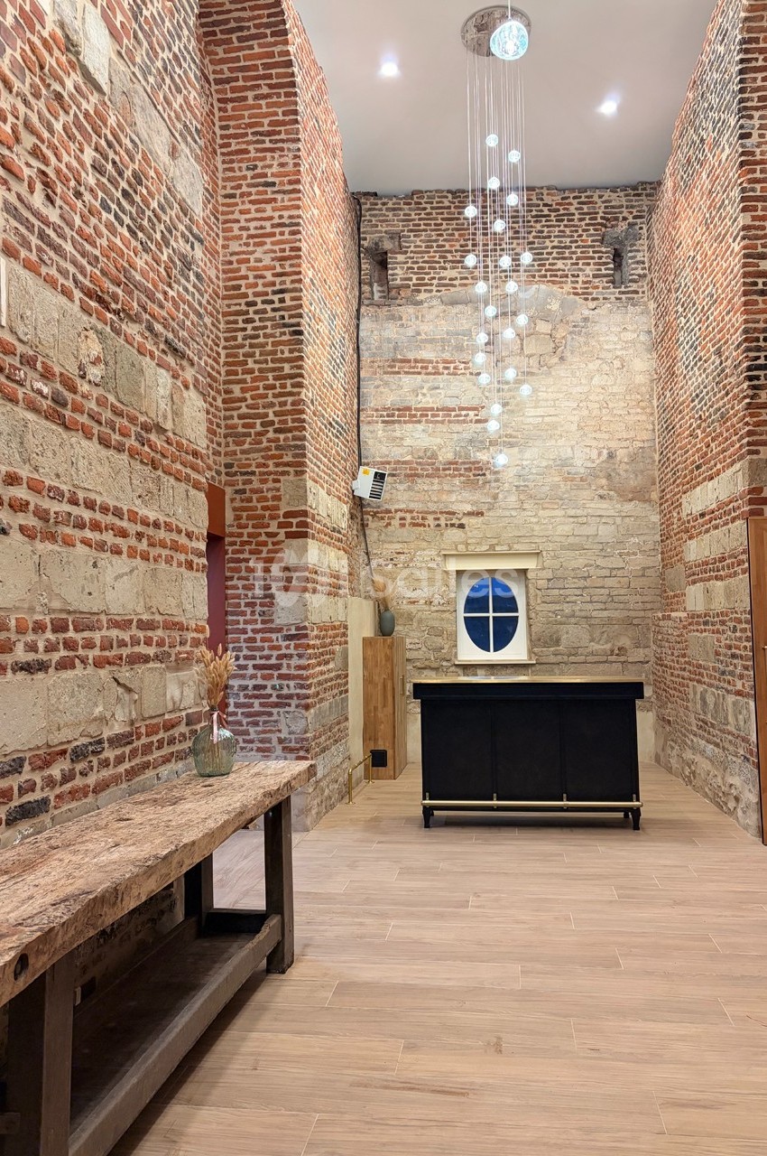 Salle en briques apparentes avec un plafond haut, un lustre moderne, un meuble noir et une table en bois rustique.