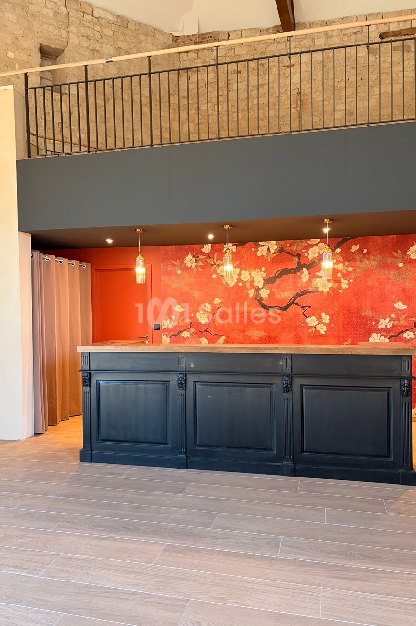 Comptoir noir devant un mur rouge décoré de motifs floraux, éclairé par des suspensions dans un espace à la décoration…