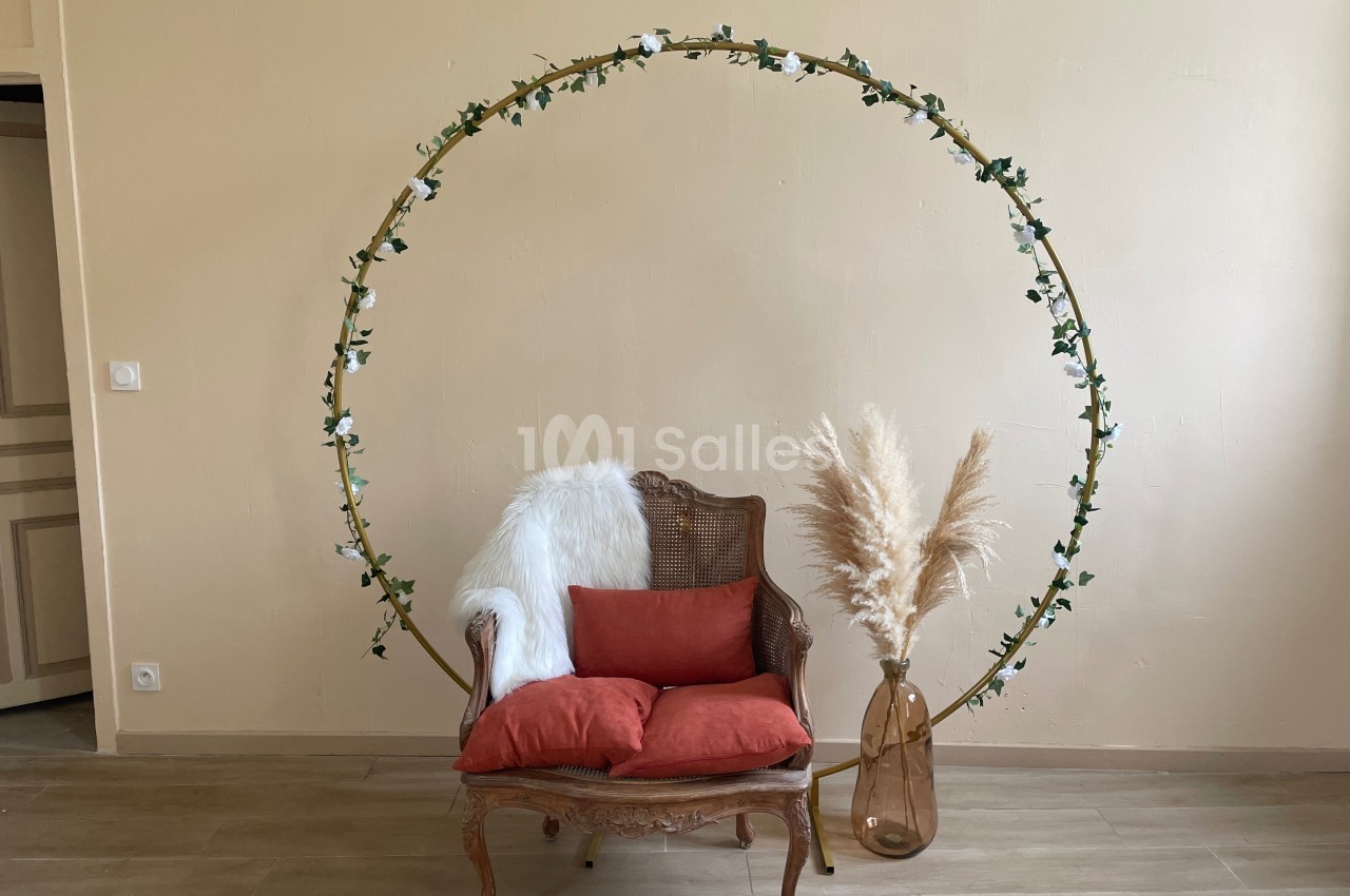 Fauteuil en osier avec coussins rouges, décoré d'un cercle floral et d'un vase contenant des herbes séchées.