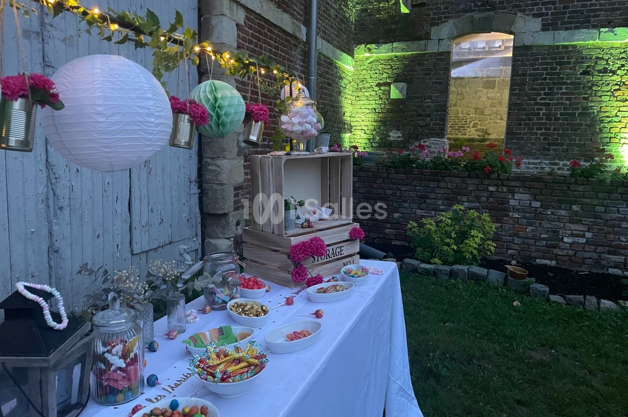 Table décorée pour un buffet de bonbons avec guirlandes lumineuses, pots en verre et éléments fleuris dans un jardin en…