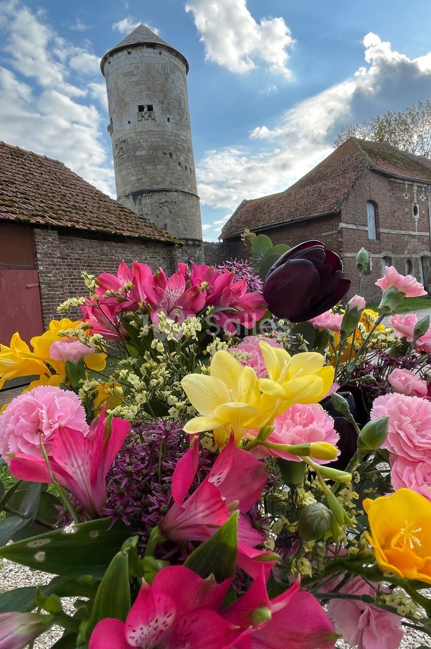Bouquet de fleurs colorées au premier plan, avec une tour en pierre et des bâtiments en briques en arrière-plan.