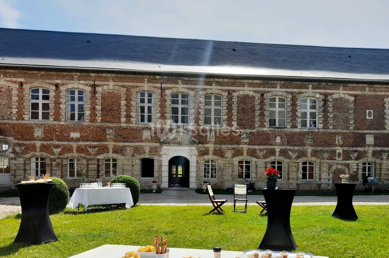 Façade en briques d'un bâtiment ancien avec tables dressées et chaises sur une pelouse ensoleillée.