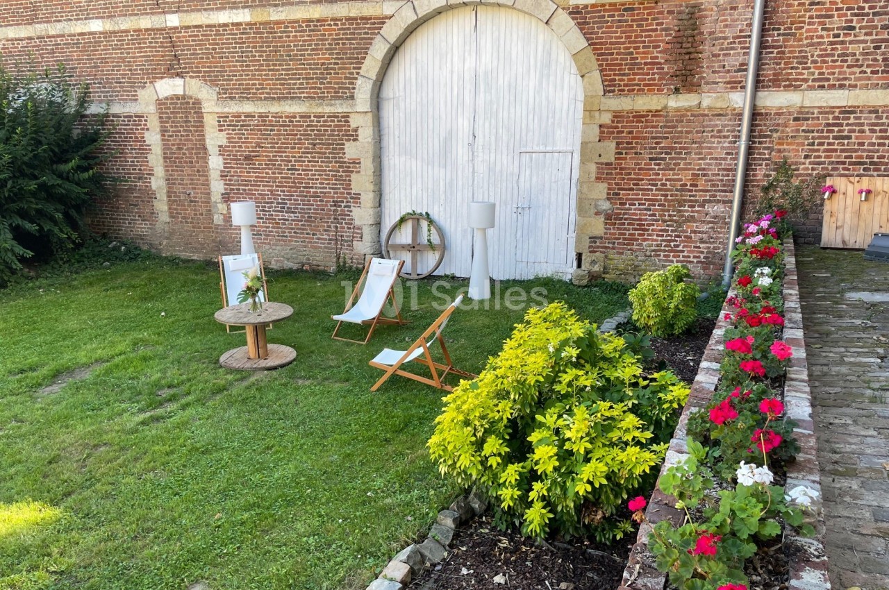 Deux chaises longues et une table basse en bois sur une pelouse près d'une porte en arc entourée de fleurs.