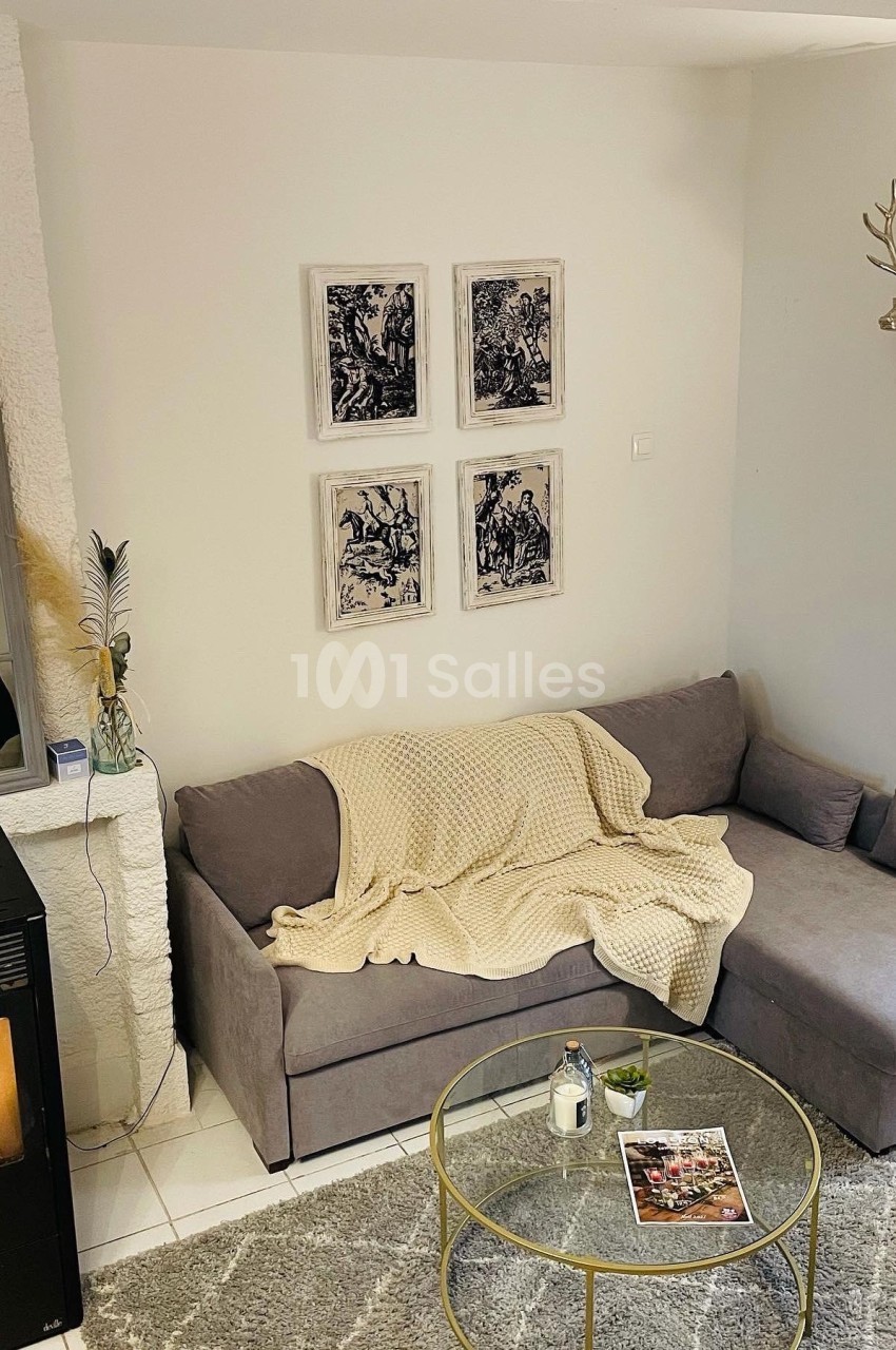 Canapé gris avec plaid beige dans un salon cosy, décoré de cadres, tête de cerf murale et table basse ronde.