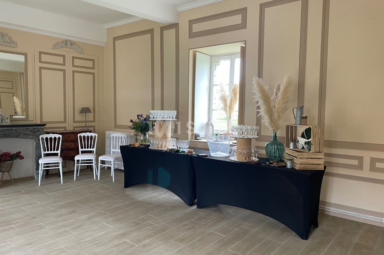 Salle élégante avec tables noires dressées pour un buffet, décorée de fleurs, pampas et caisses en bois près d'une fenêtre.