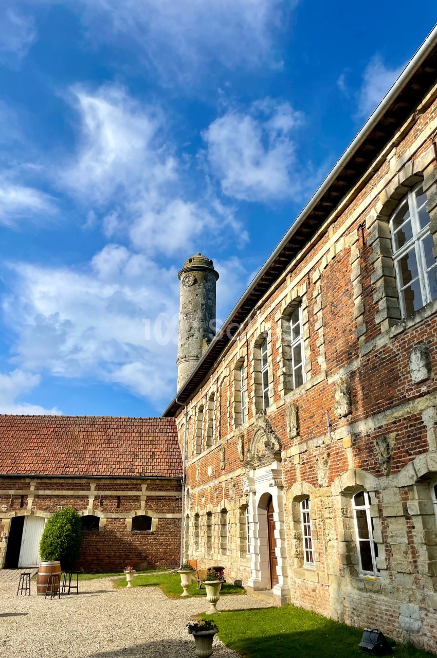 Bâtiment en briques rouges avec une tour en pierre, sous un ciel bleu parsemé de nuages.
