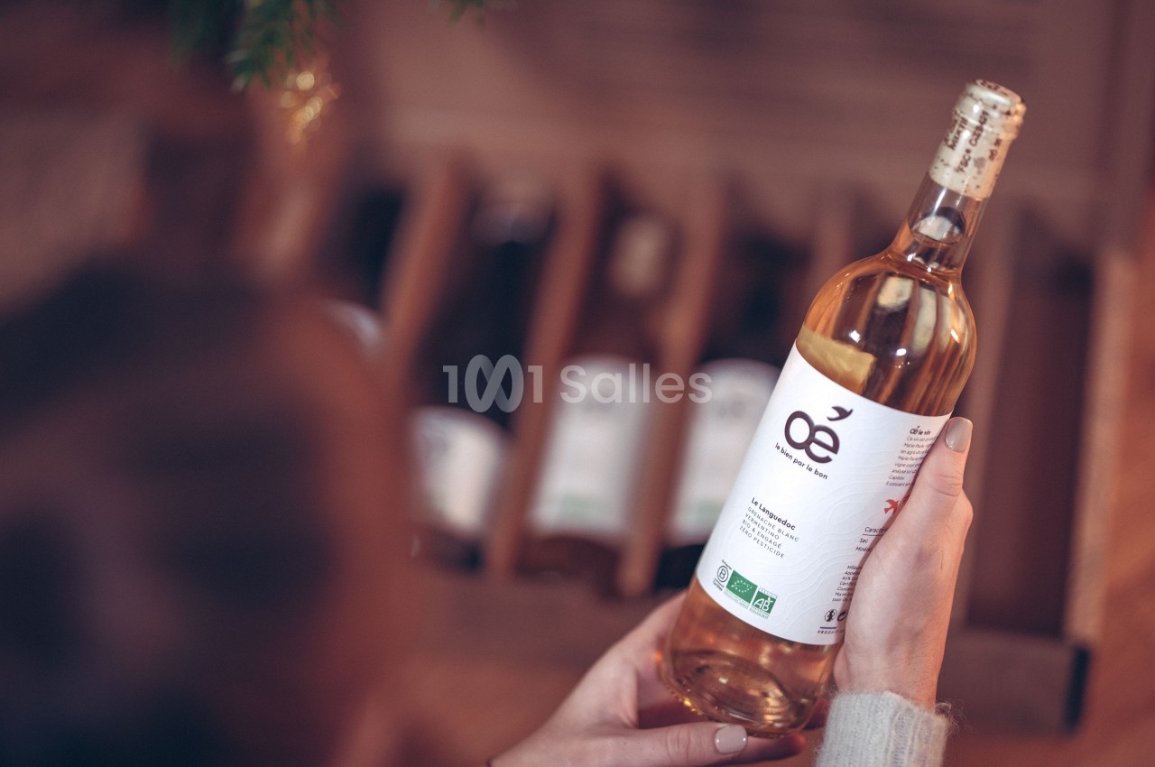 Une personne tient une bouteille de vin blanc biologique devant une caisse contenant d'autres bouteilles.