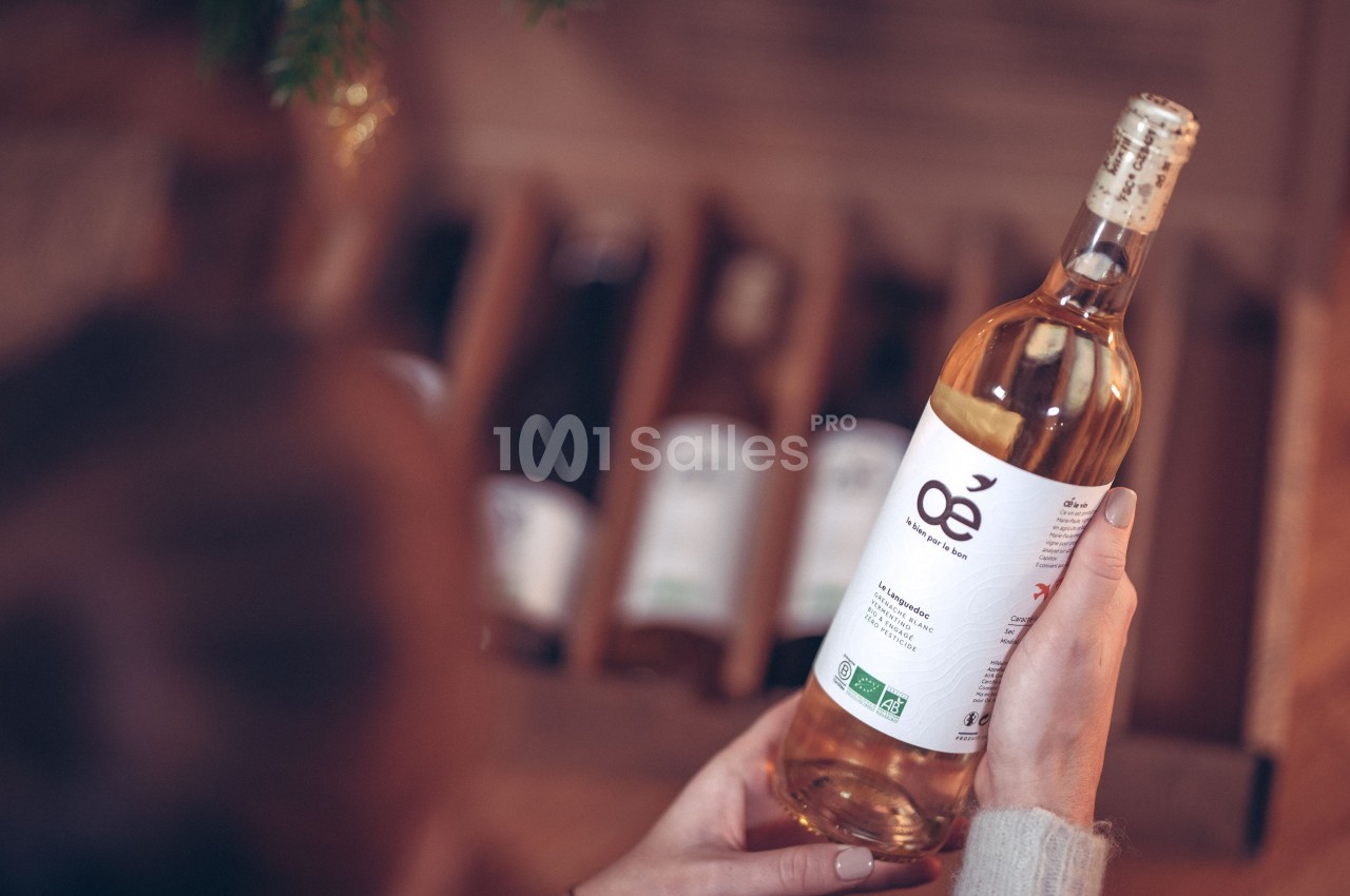 Une personne tient une bouteille de vin blanc biologique devant une caisse contenant d'autres bouteilles.