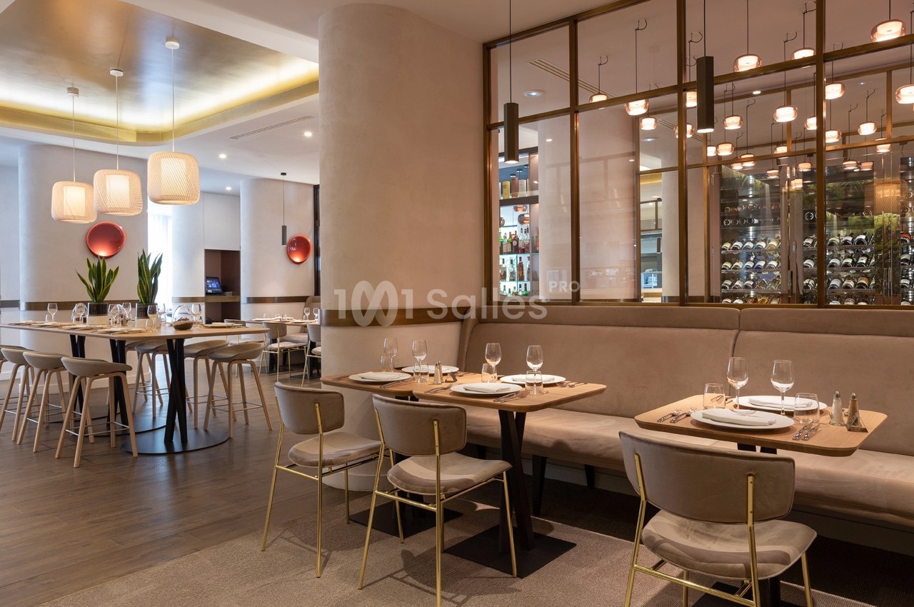 Salle de restaurant moderne avec tables dressées, chaises rembourrées et éclairage suspendu chaleureux.