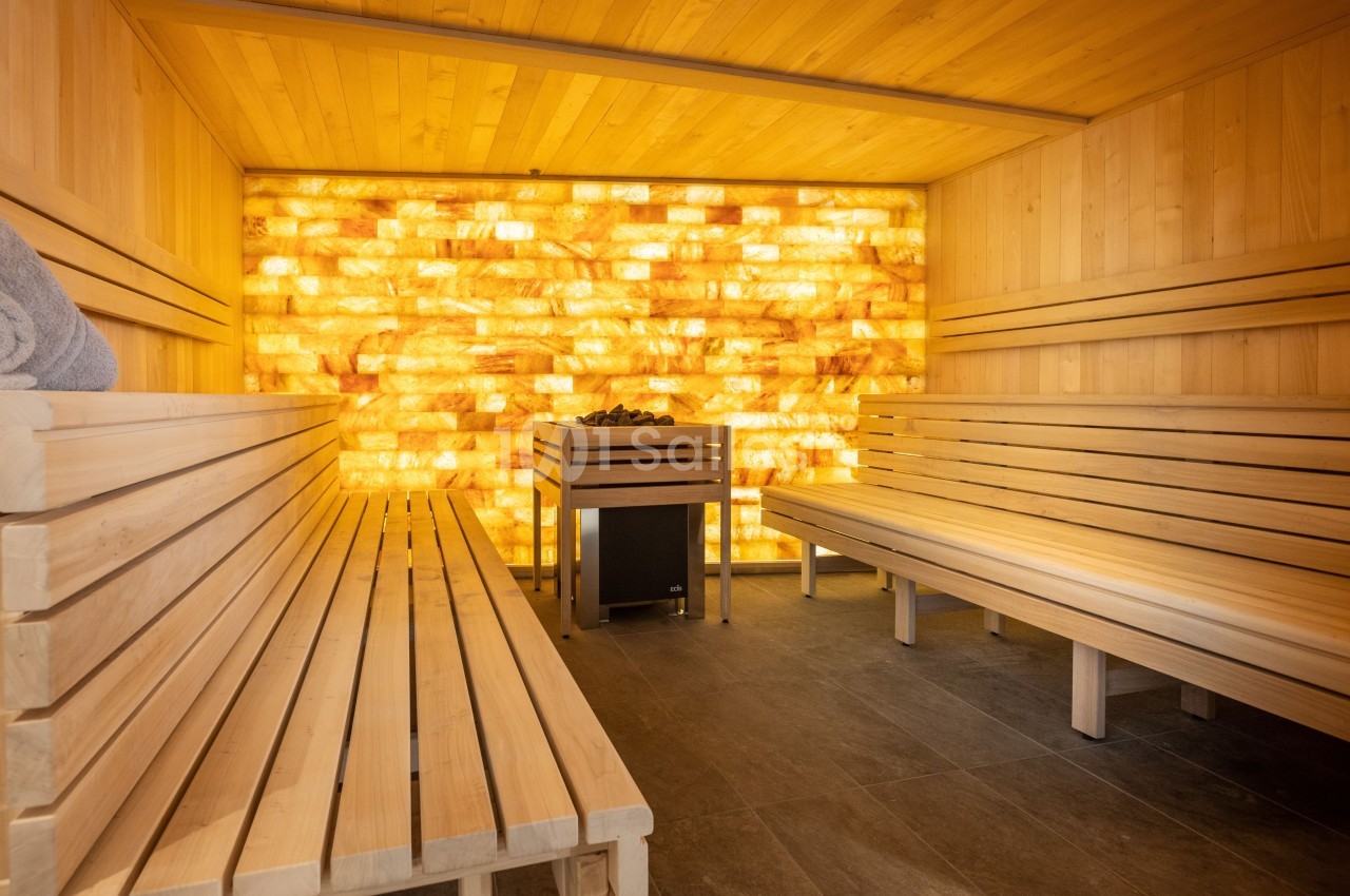 Intérieur d'un sauna en bois avec un mur rétroéclairé en briques de sel et des bancs alignés de chaque côté.