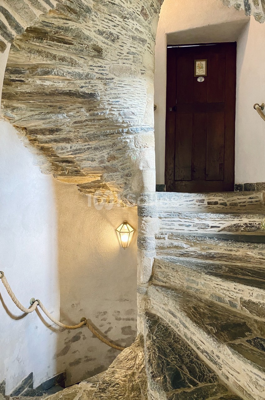 Escalier en pierre en colimaçon avec des murs blancs, une rampe en corde et une porte en bois en haut.