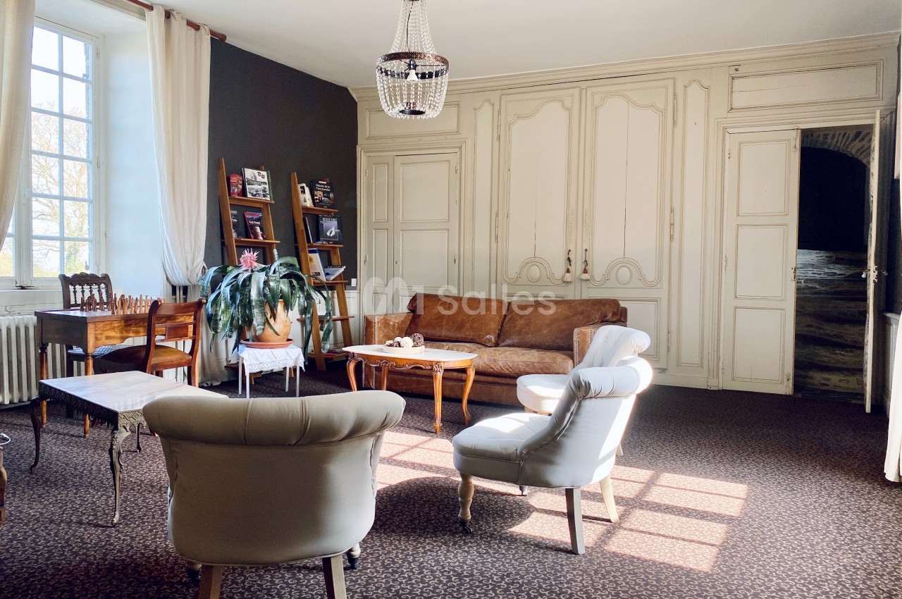 Salon lumineux avec canapé en cuir, fauteuils blancs, table basse en bois, étagères et grande fenêtre.