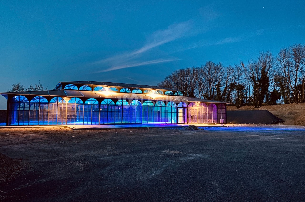 Bâtiment vitré illuminé par des lumières colorées dans un paysage nocturne avec des arbres en arrière-plan.