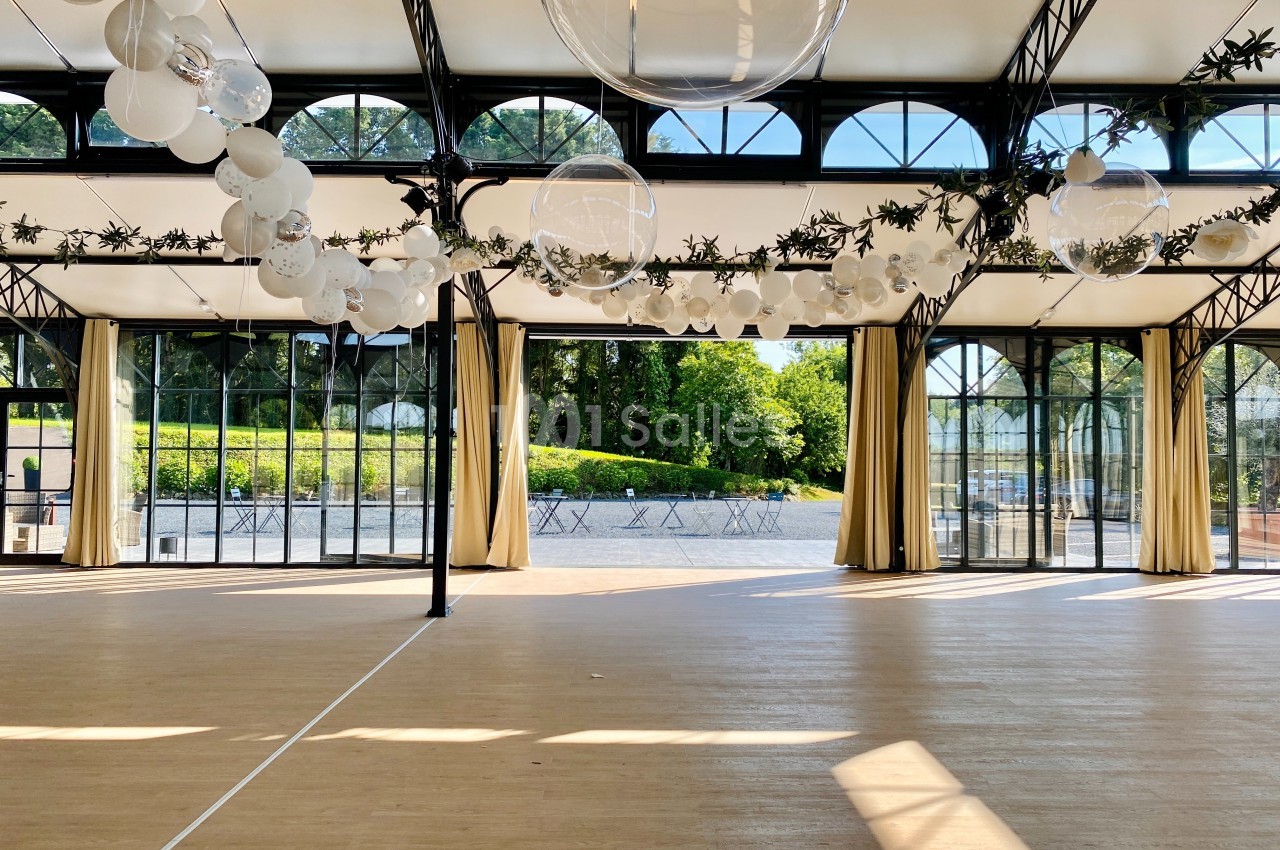 Salle lumineuse avec de grandes baies vitrées, des rideaux beiges et une décoration suspendue composée de globes et de…